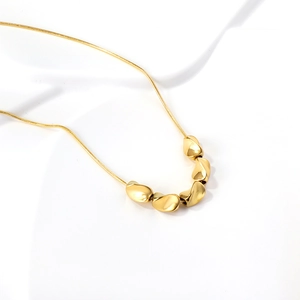 Minimalist gold snake chain necklace with irregular pebble charms on white fabric