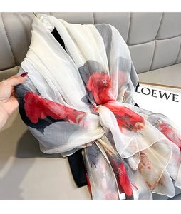 Close-up of translucent fabric with elegant red floral patterns on a white silk scarf