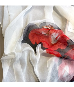 Detail of elegant white silk scarf featuring red floral patterns and textured grid fabric