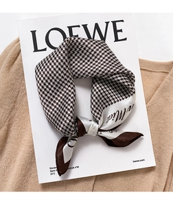 Detail of houndstooth silk scarf with cursive letter design on a beige knit background