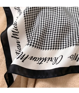 Detailed close-up of a houndstooth silk scarf showing elegant texture and lettering