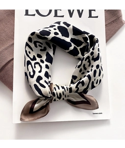 Detail view of stylish leopard print silk scarf tied in a bow on a white magazine