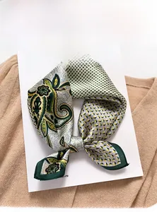 Close-up of a premium silk paisley square scarf folded elegantly on a beige sweater