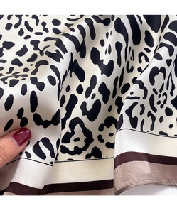 Close-up of leopard print silk scarf showing satin texture and striped edge borders