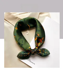 Detail of green silk scarf with vintage floral prints tied on a beige shirt collar