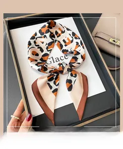 Detail of silk leopard print skinny scarf with artistic letters tied in a bow on a handbag