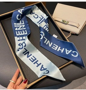 Blue and grey letter print silk twilly scarf styled on a luxury beige leather handbag