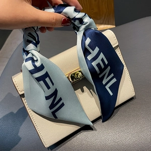 Detail of a beige pebbled leather handbag with an elegant blue printed silk scarf handle