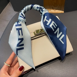 Detail of a beige leather handbag handle wrapped with a printed silk scarf and gold lock