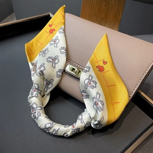 Floral print silk scarf with yellow edges wrapped around a leather handbag handle