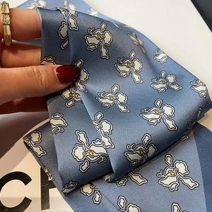 Detailed macro view of light blue silk scarf with white floral patterns and soft drape