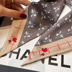 Close-up of narrow twilly scarf with dark grey floral pattern and red heart line edge