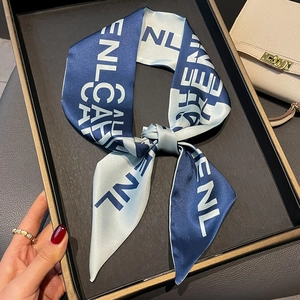 Blue satin silk scarf with white letter prints tied as a bow on a luxury tray
