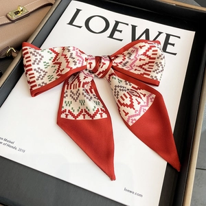 Detail of red geometric silk scarf tied in a bow on a white prop with satin finish