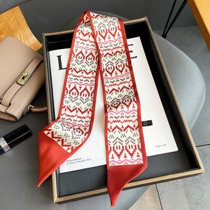 Macro detail of a long silk twilly scarf with red borders and geometric ethnic patterns
