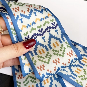 Detail of a pixelated geometric pattern scarf with blue edge stitching and silky texture