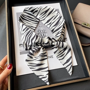 Foulard twilly en soie à motif zèbre noué en boucle sur un sac à main beige chic