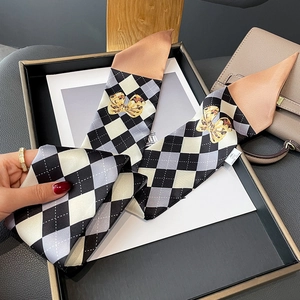 Détail d'un foulard étroit en soie avec motifs de losanges et imprimés nœuds dorés