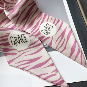 Détail macro d'un foulard en satin à motif zèbre rose et beige avec logo Grace