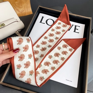 Detail view of a floral silk scarf with caramel edges on a white display card