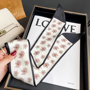 Close-up of floral print silk twilly scarf with black edges on a beige leather bag