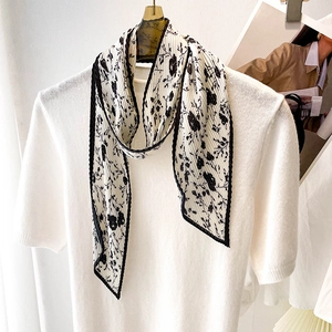 Détail d'un foulard plissé à fleurs blanc cassé avec bord noir sur un haut en tricot
