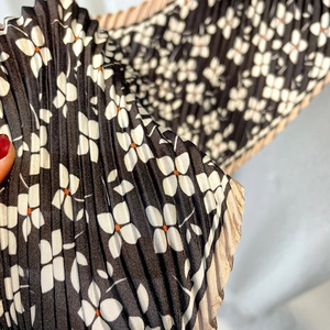 Macro detail of pleated floral scarf showing white flower patterns and golden edges