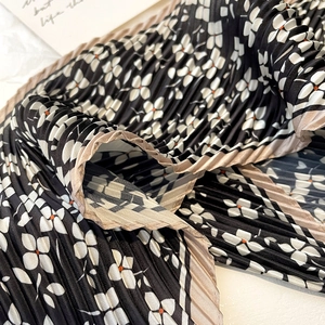 Detailed view of micro-pleated floral scarf with black white and orange petal patterns
