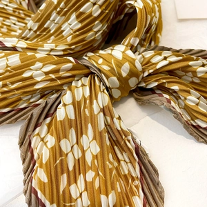 Detailed macro view of yellow floral pleated silk scarf with fine texture and piping