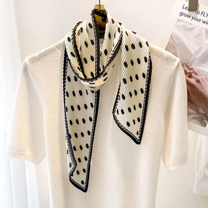 Detail of polka dot pleated scarf in cream white with black trim on a gold hanger