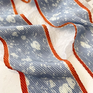 Détail d'un foulard plissé bleu à fleurs avec une bordure orange contrastante
