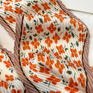 Detail of accordion pleated floral scarf featuring orange petals and green leaves print
