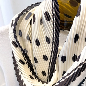 Detail of black polka dot pleated silk scarf with stripe edge on white sweater