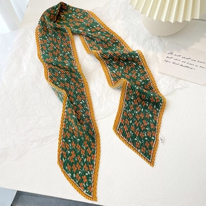 Close-up of pleated silk scarf with green floral pattern and orange flower prints