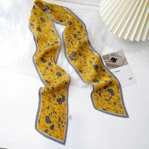 Détail d'un foulard en soie plissé jaune avec imprimés floraux bleus et bords dentelés