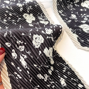 Détail d'un foulard en soie plissé noir avec imprimé roses blanches et texture fine