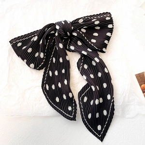 Close-up of pleated black polka dot scarf featuring white contrast stitching and bow style