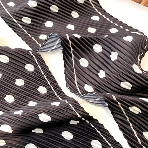 Detail of pleated polka dot silk scarf featuring white patterns on black fabric texture