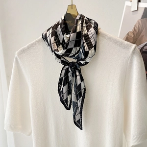 Detail of pleated silk scarf with black, white and brown diamond pattern on white knitwear