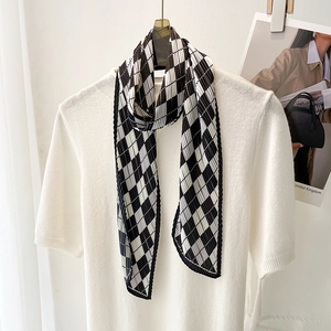 Detail of pleated black and white checkered silk scarf tied on a white knit sweater