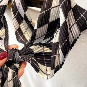 Detail showing pleated black and white diamond plaid scarf tied in a stylish knot