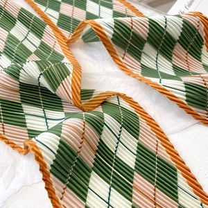 Macro detail of pleated diamond check silk scarf in green and beige with orange hem