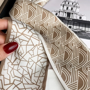 Détail des motifs géométriques marron et blanc recto-verso sur le long foulard étroit