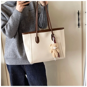 Dettaglio di una grande borsa tote crema con manici marroni e ciondolo a forma di orso