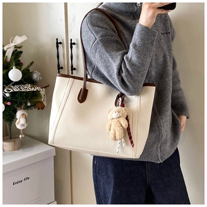 Dettaglio borsa tote color crema con manici marroni e ciondolo a forma di orsetto su modella