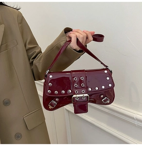 Detalle del bolso baguette de charol burdeos con remaches y hebilla de metal