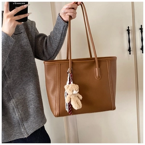 Dettaglio della borsa tote in pelle marrone martellata con un ciondolo a forma di orsetto