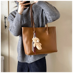 Dettaglio di una borsa tote grande in pelle marrone con ciondolo a forma di orsetto