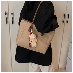 Dettaglio della borsa tote beige con trama litchi, bordo marrone e ciondolo a forma di orso