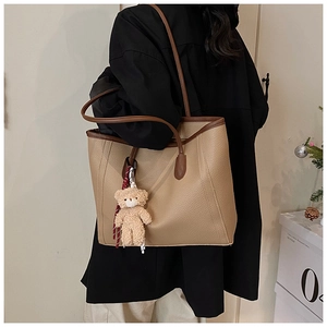 Dettaglio della borsa tote in pelle kaki a grana litchi con bordi marroni e ciondolo a orso
